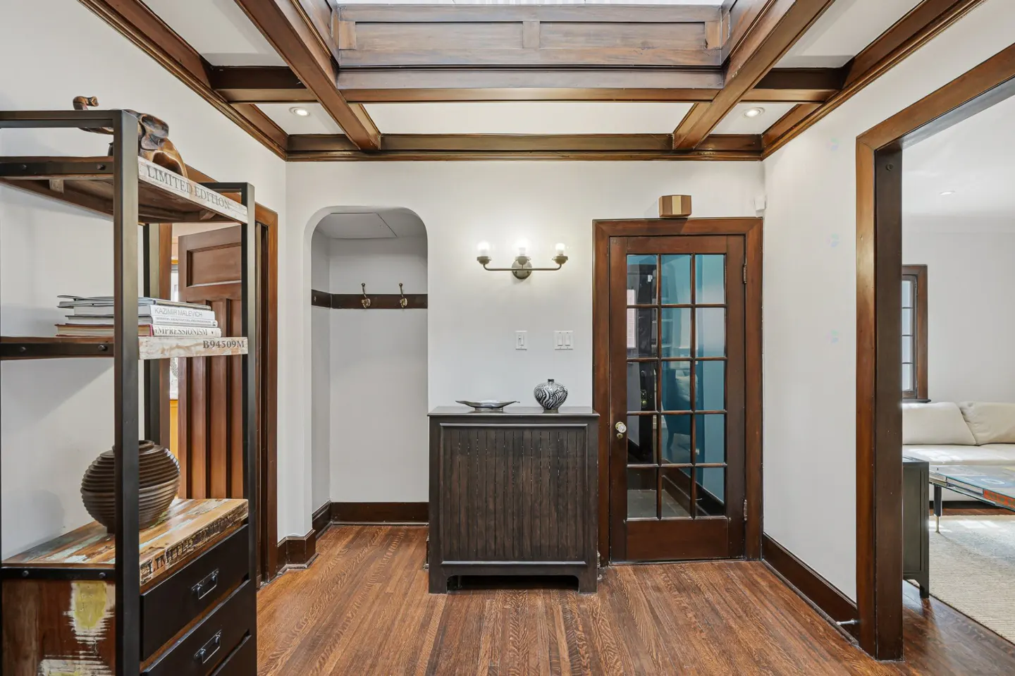 Entryway with hardwood floors, white walls, and dark wood trim. A cabinet sits below a light fixture, and a glass-paneled door is to the right.