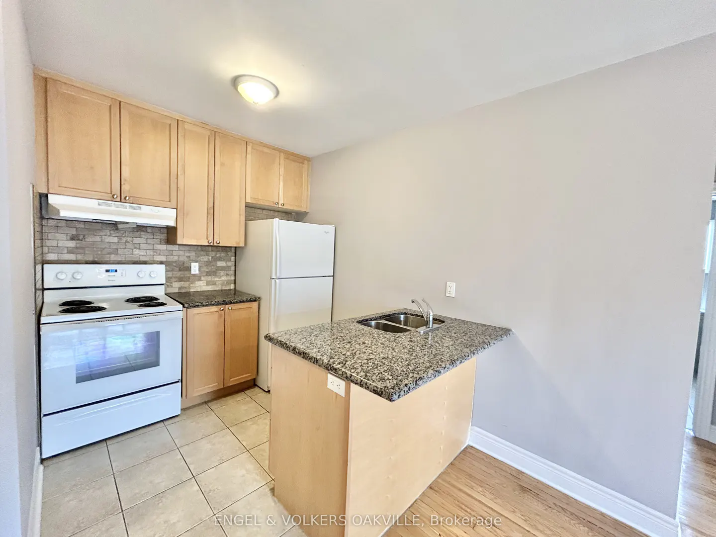 A kitchen with light wood cabinets, a white stove and refrigerator, and a granite countertop island.