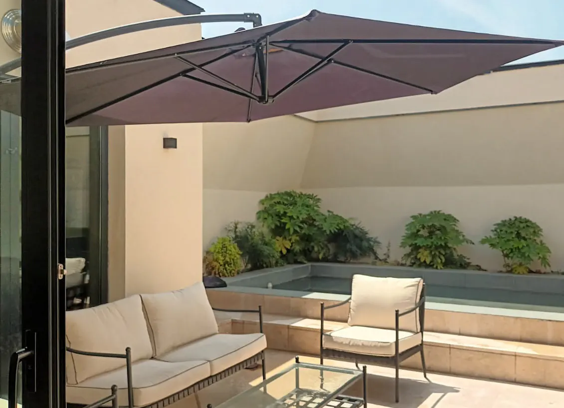 Outdoor patio with a pool, lounge chair, and sofa under a large brown umbrella.