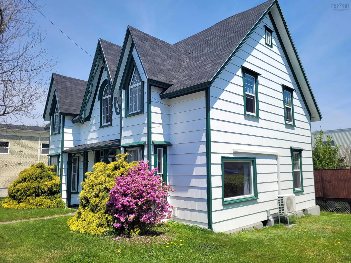 Exterior view of a two-story white house with green trim and a dark gray roof on a sunny day.