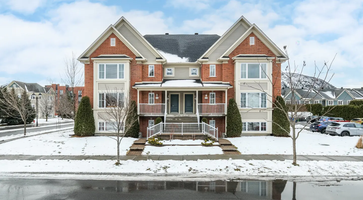 Two-story brick townhouse with white trim, balconies, and a black roof, set in a snowy landscape under a blue sky.