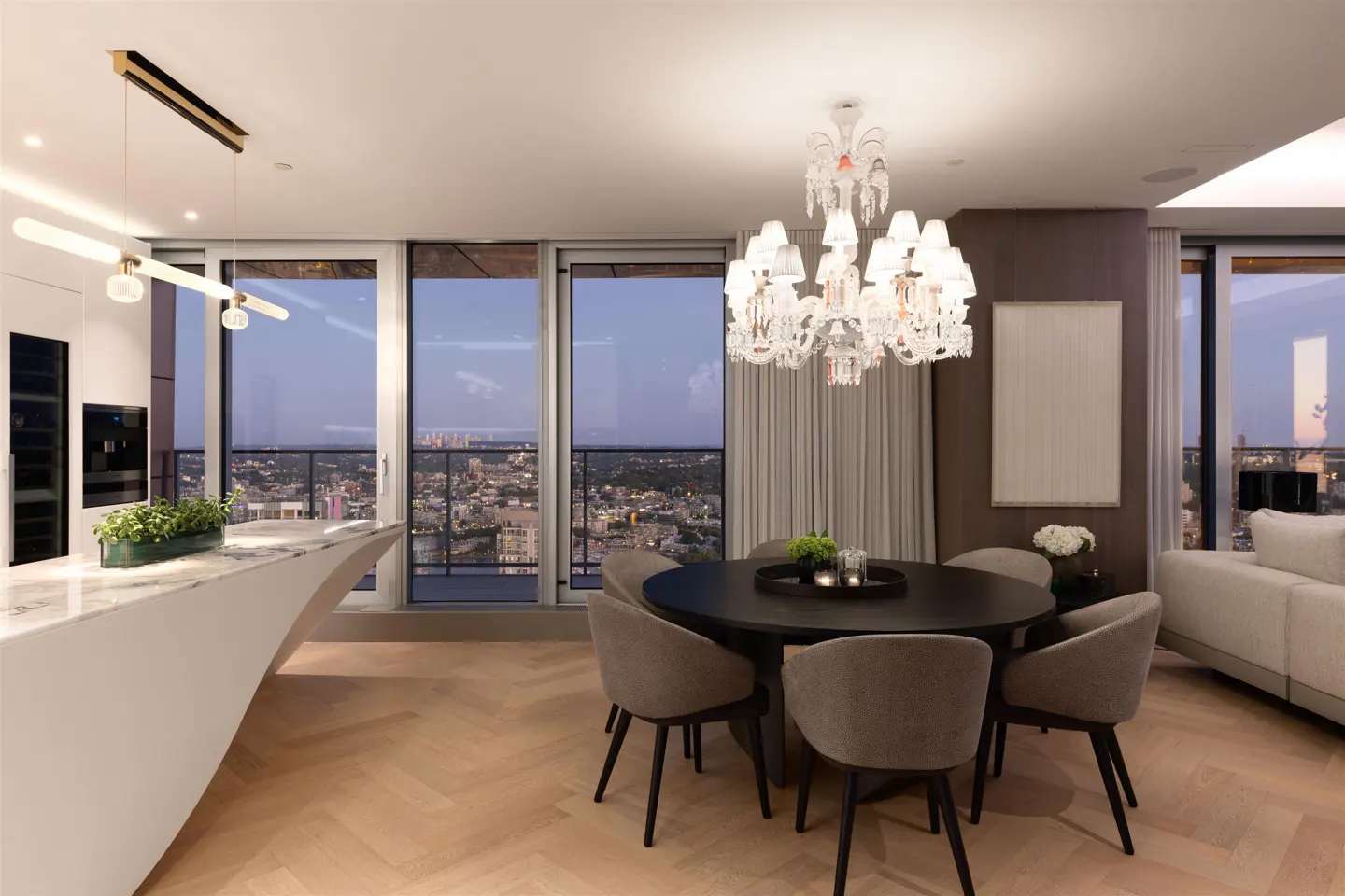 Modern apartment interior with a round dining table, chandelier, and city view at dusk.
