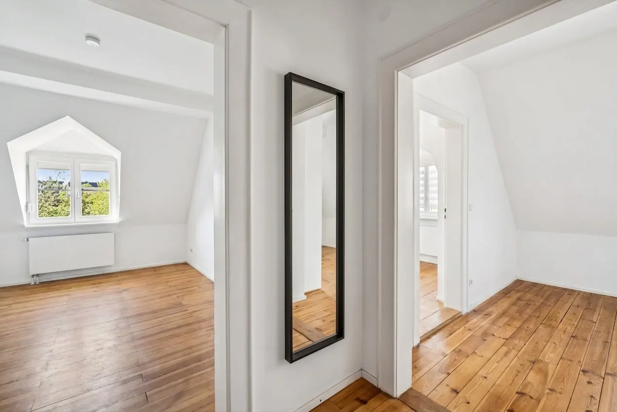Hallway with hardwood floors, white walls, and two doorways. A black-framed mirror hangs on the wall between the doorways.