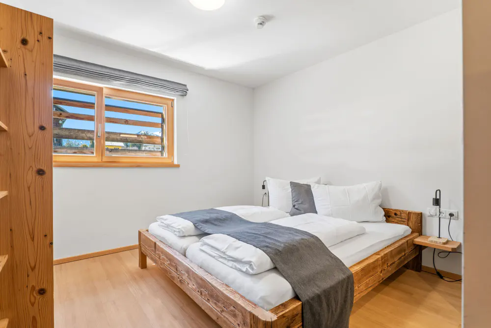 Bedroom with wooden bed frame, white walls, and wood floors. A window with a view is on the left.