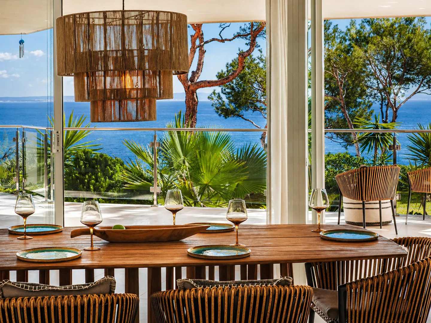A dining room with a wooden table, wicker chairs, and a view of the ocean.