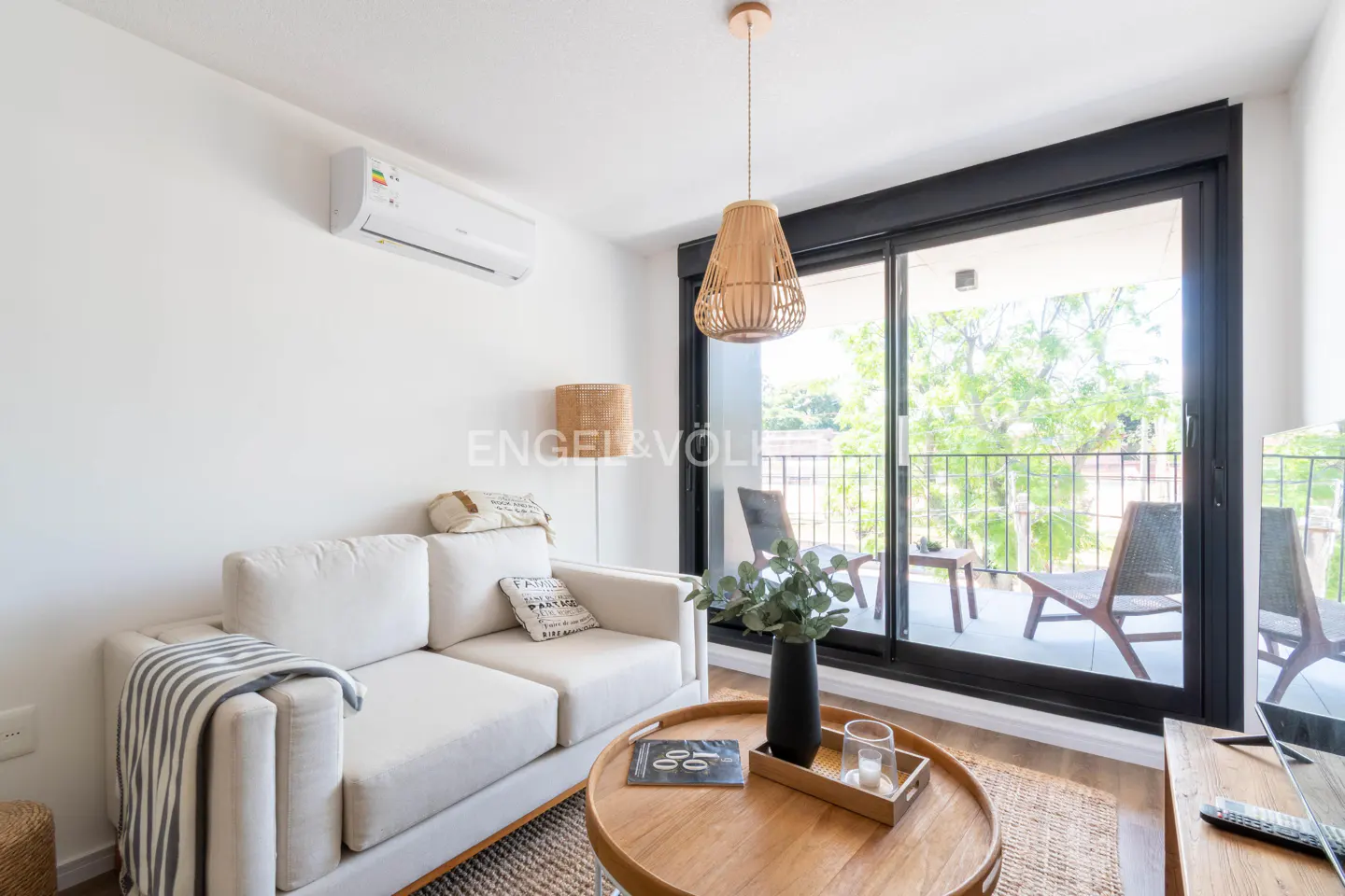 Bright living room with white sofa, wood table, and balcony with chairs visible through sliding glass doors.
