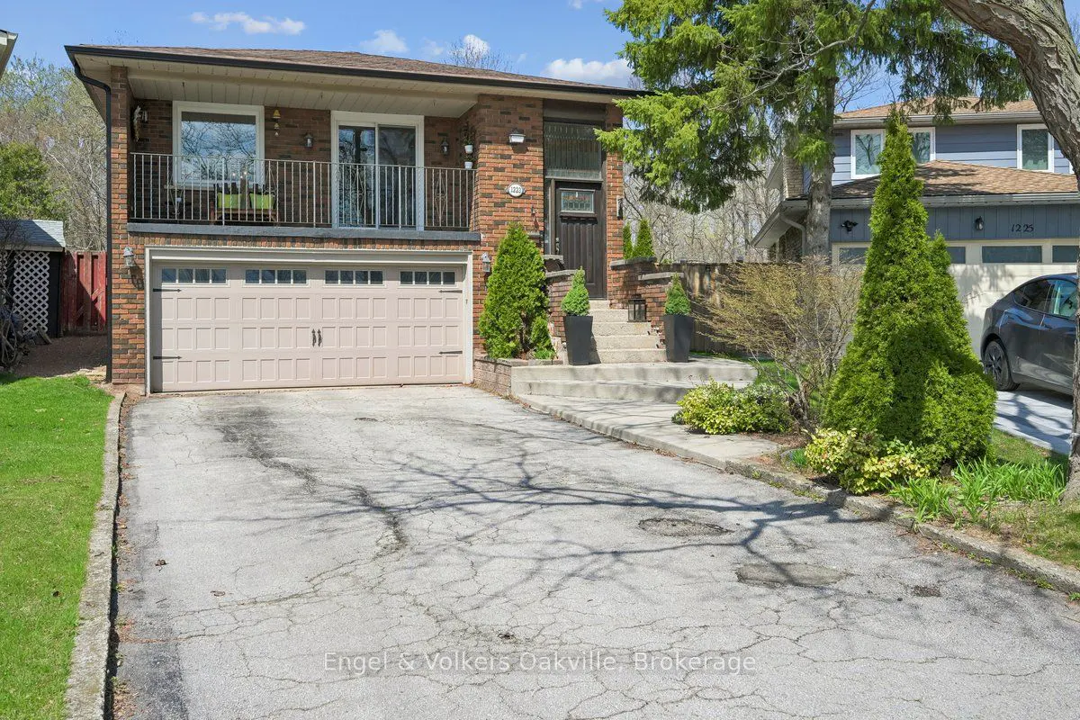 Two-story brick house with a balcony, beige garage door, and concrete steps leading to a dark brown front door.