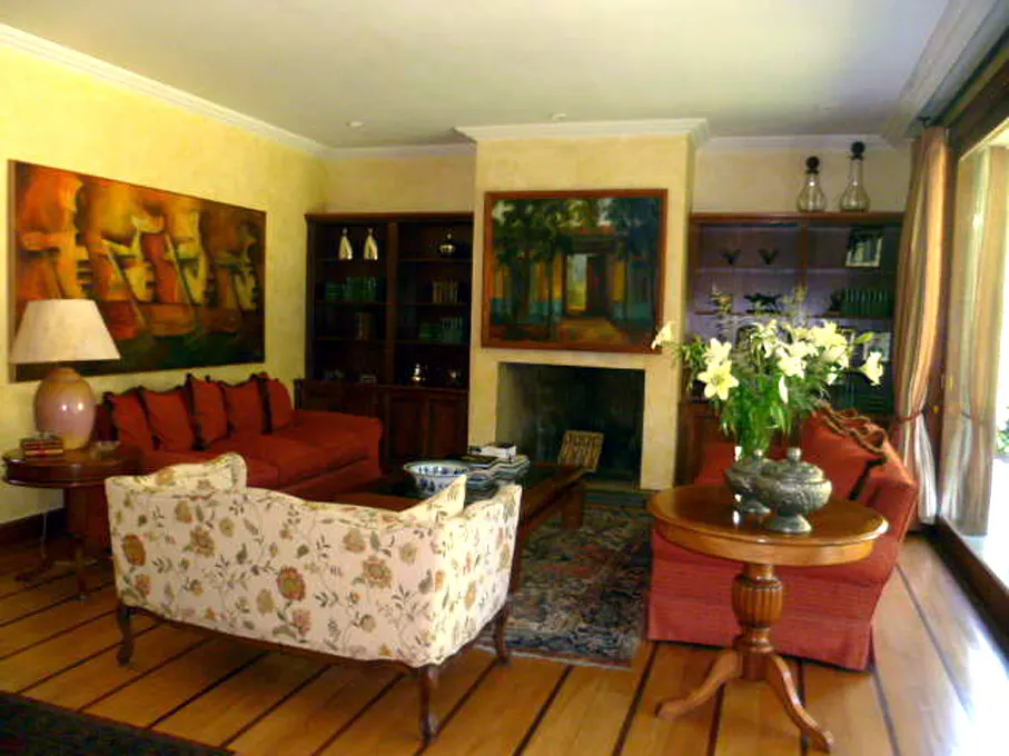 Living room with hardwood floors, floral sofa, red couch, and fireplace. Art hangs above the fireplace and on the wall.