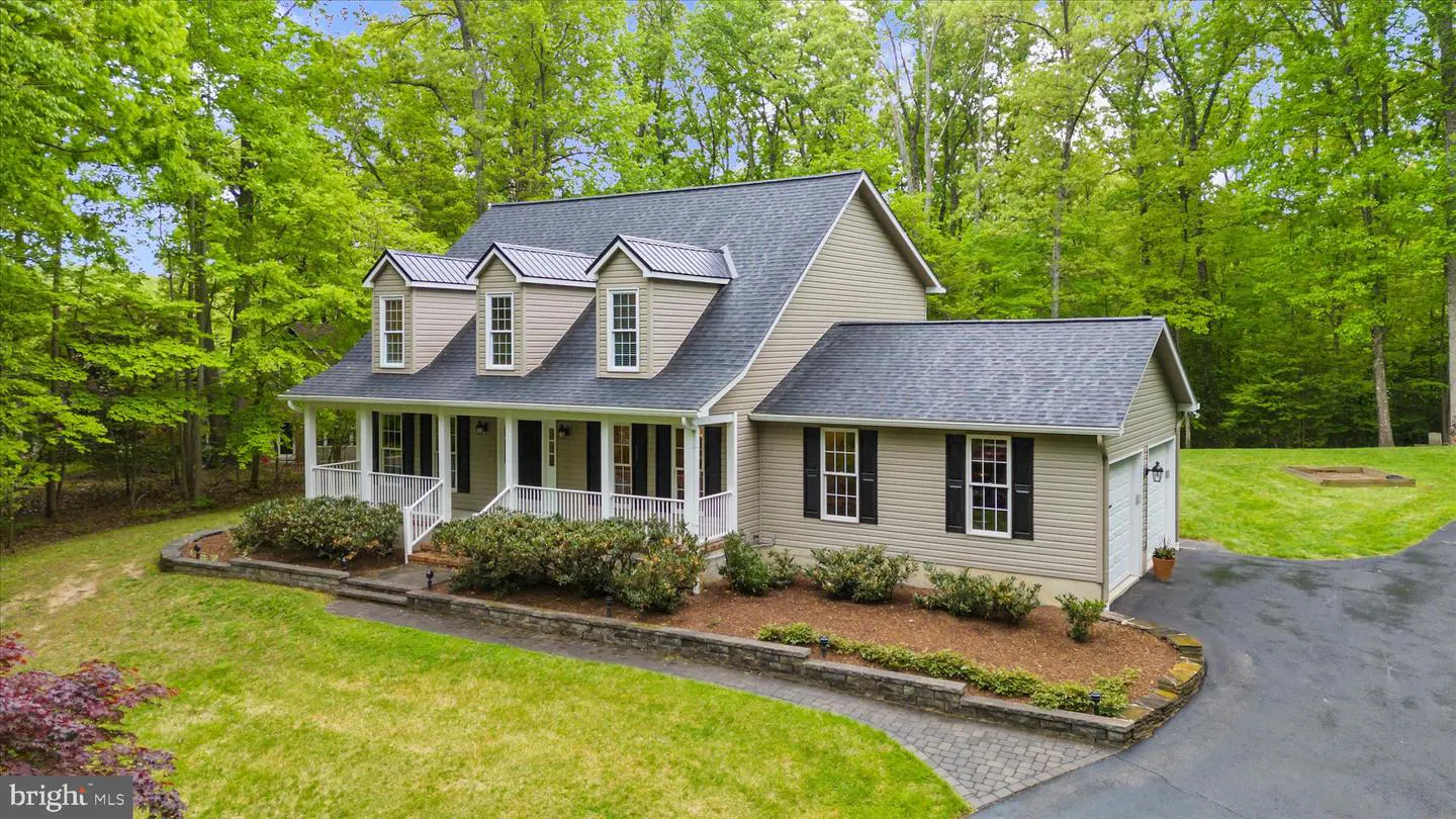 Tan two-story house with a gray roof, white trim, and black shutters surrounded by green trees and lawn.