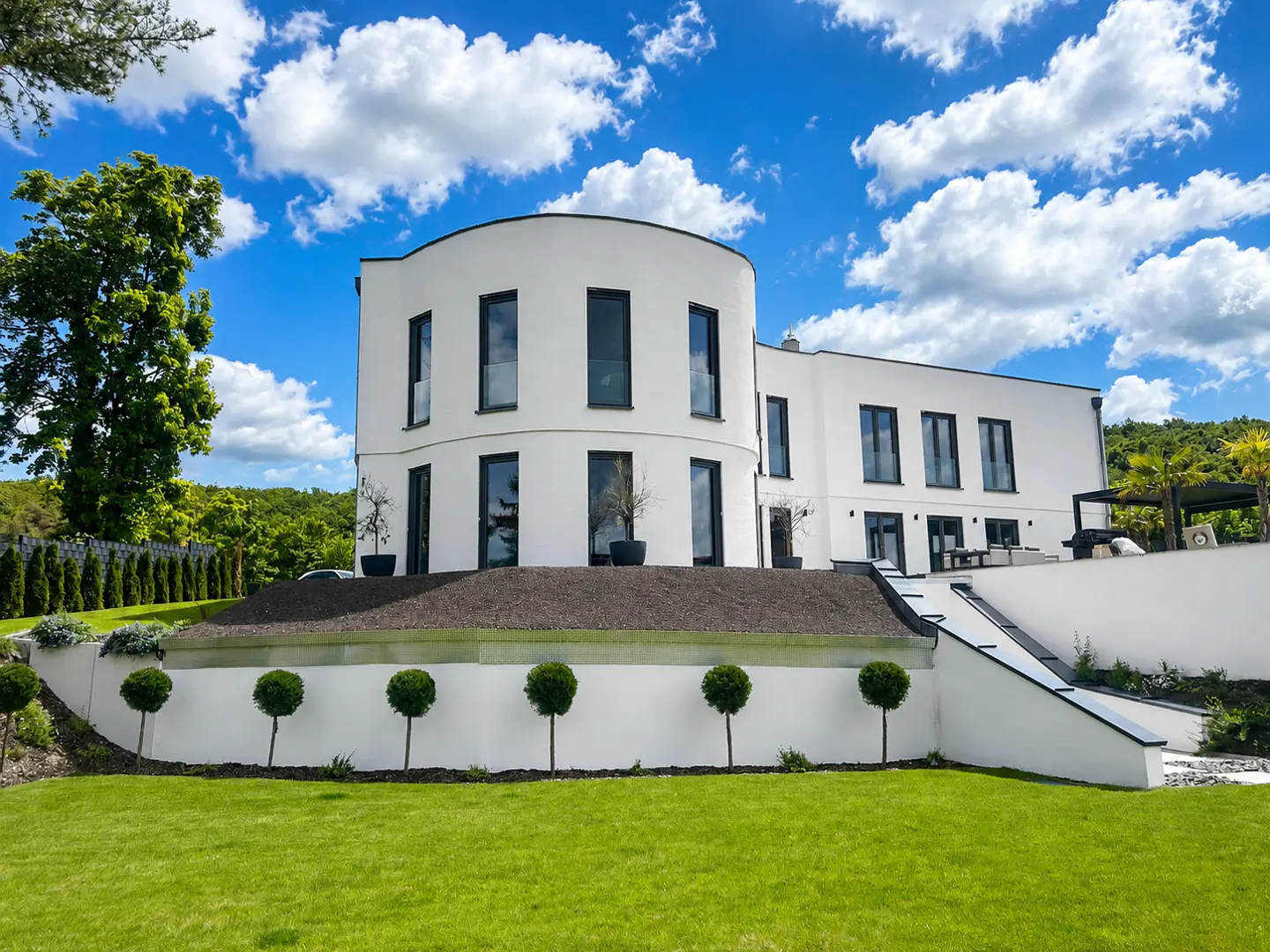 Modern white house with black framed windows, green lawn, and blue sky with white clouds.
