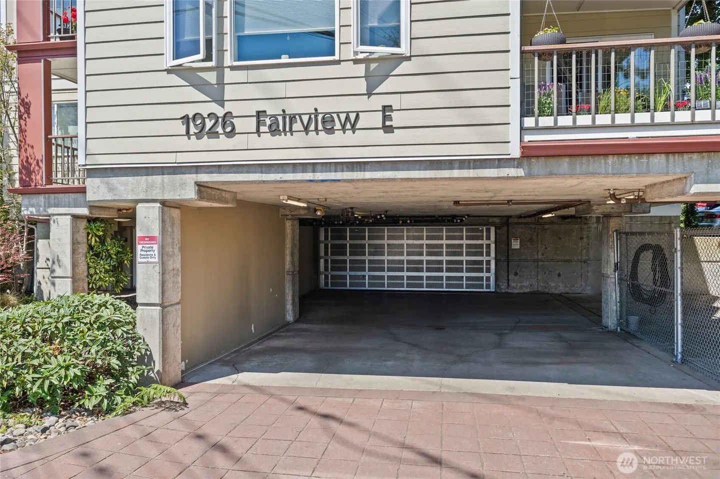 Exterior view of a tan apartment building at 1926 Fairview E with a covered ground-level parking garage and paved driveway.