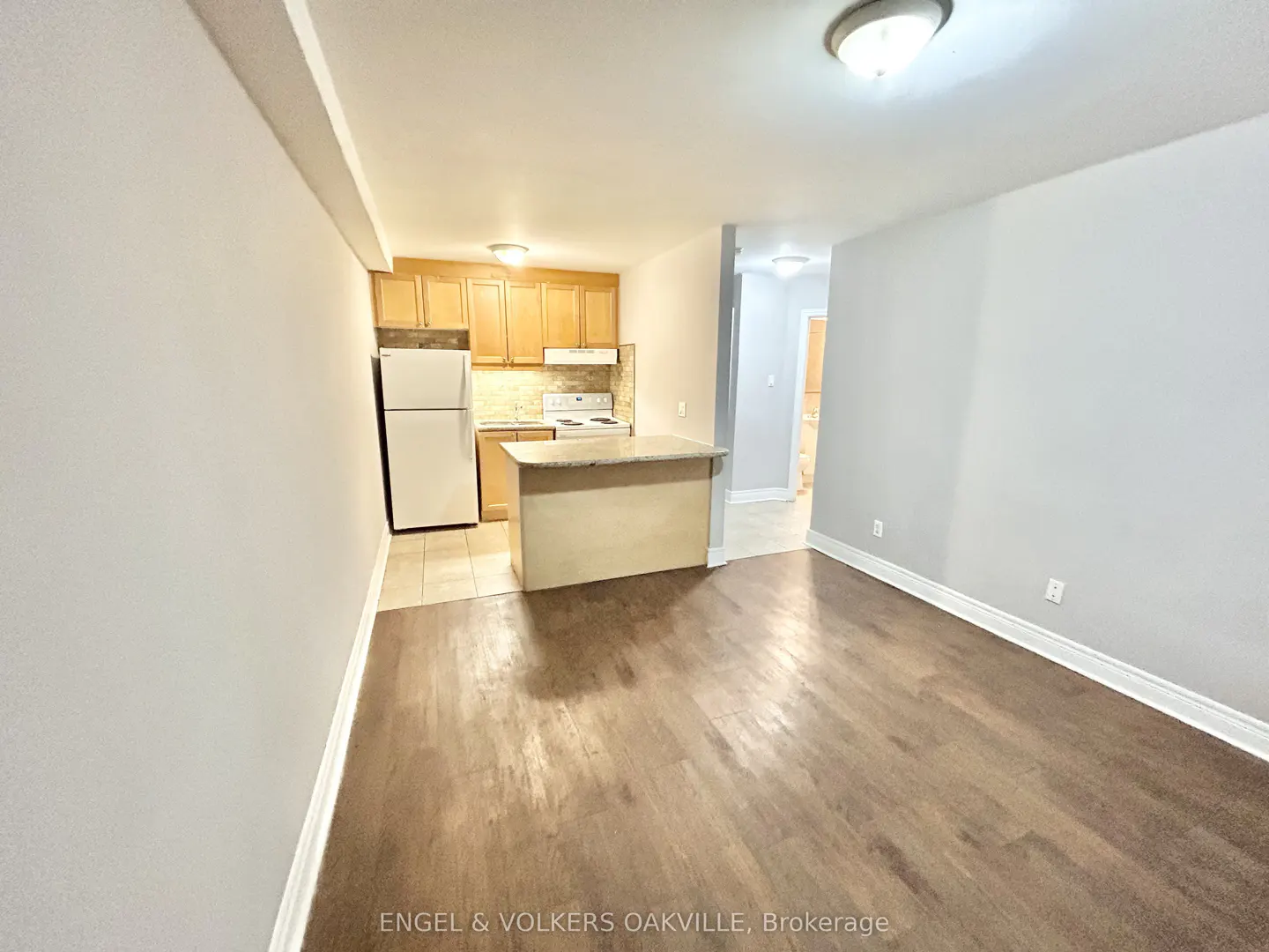 Open-concept kitchen with light wood cabinets, white appliances, and a breakfast bar, overlooking a spacious living area.
