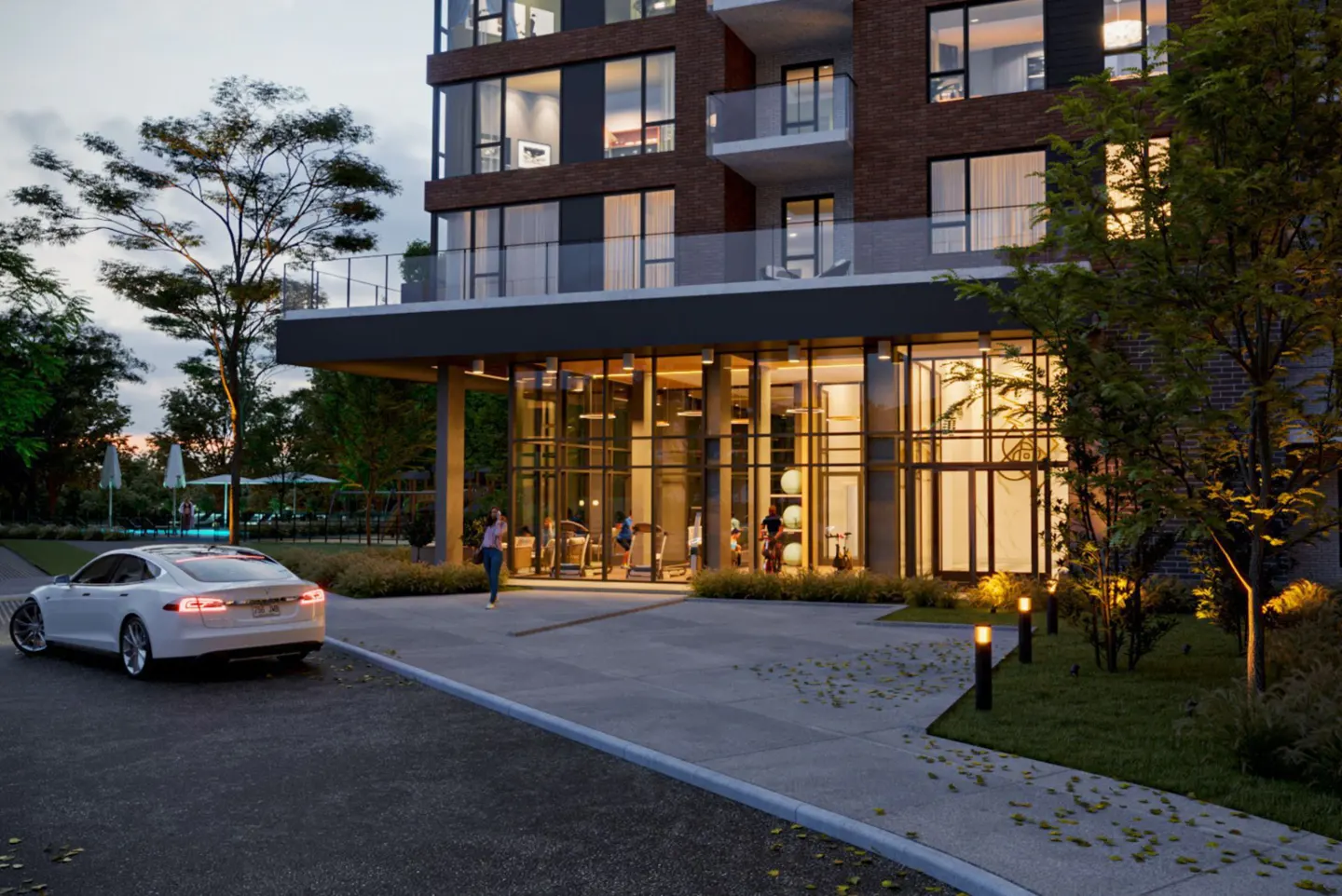 Modern brick apartment building with a glass-enclosed lobby and a white Tesla parked in front. A pool is visible in the background.