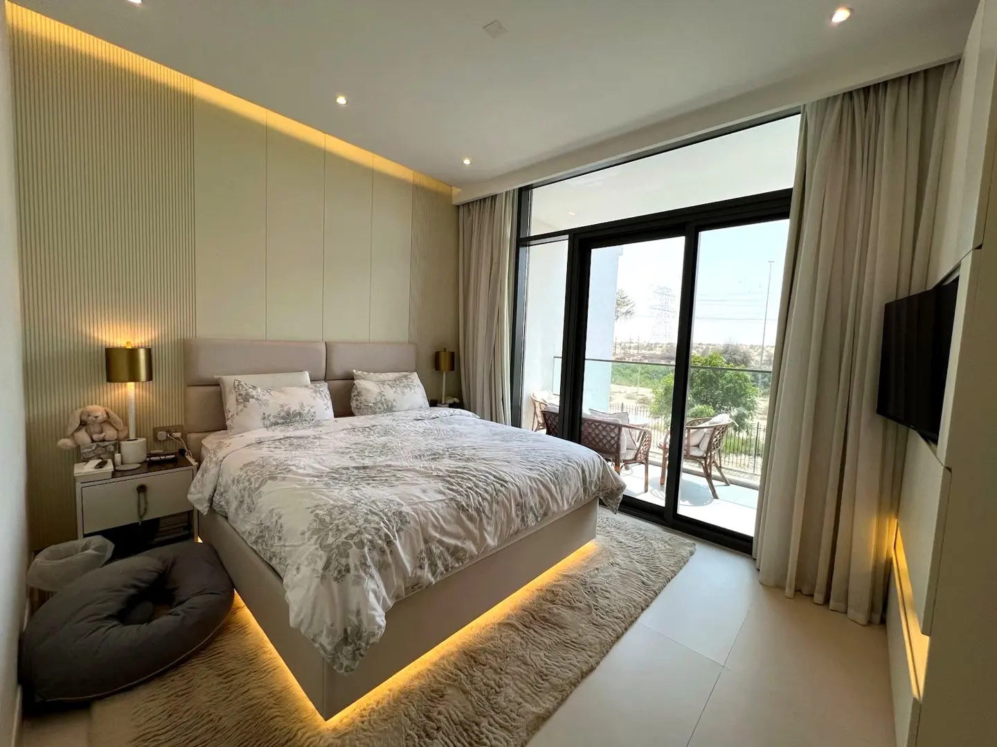 Modern bedroom with a king bed, floral bedding, under-bed lighting, and a balcony with outdoor seating.