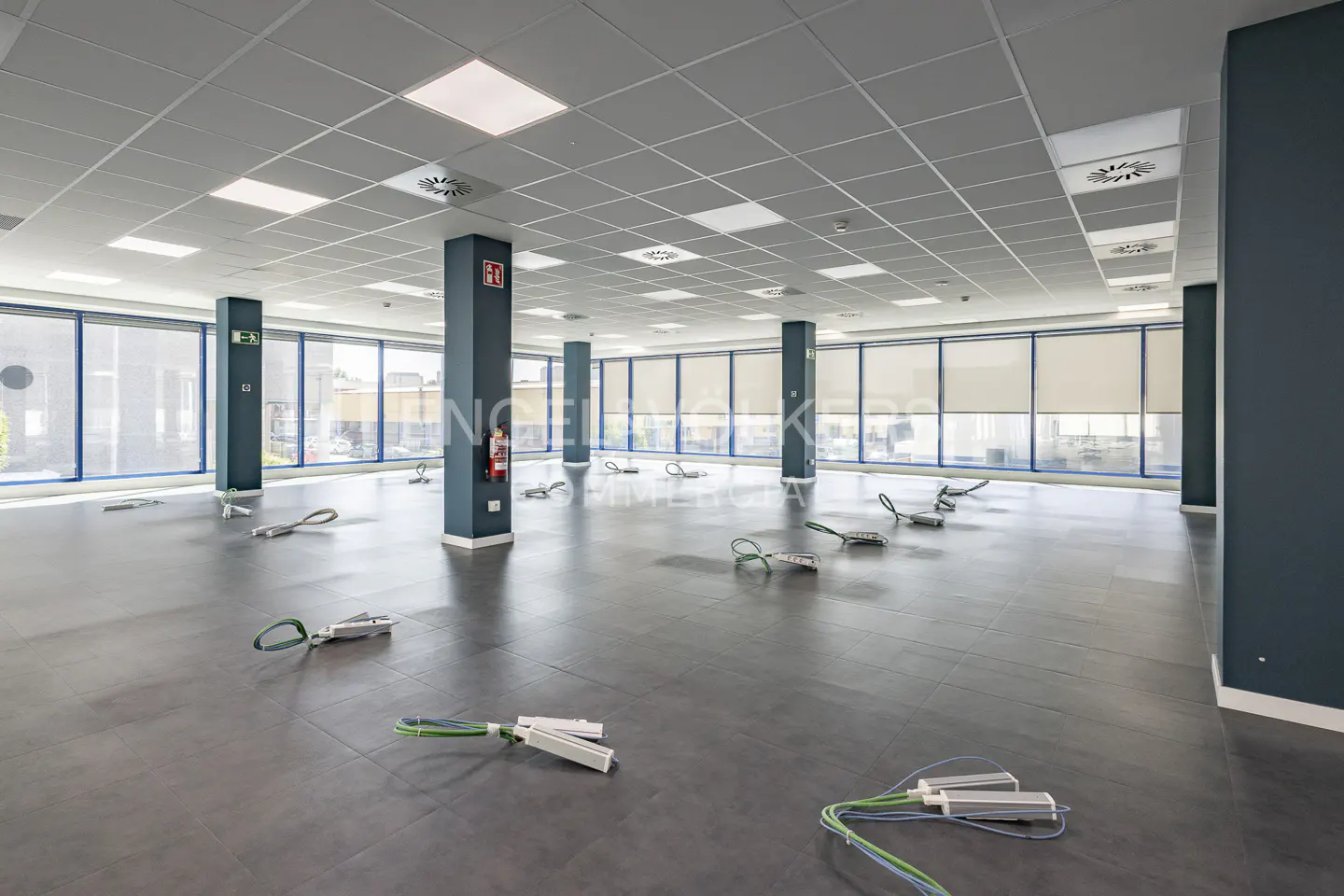 Empty modern office space with dark grey tiled floors, large windows, and exposed electrical cables on the floor.