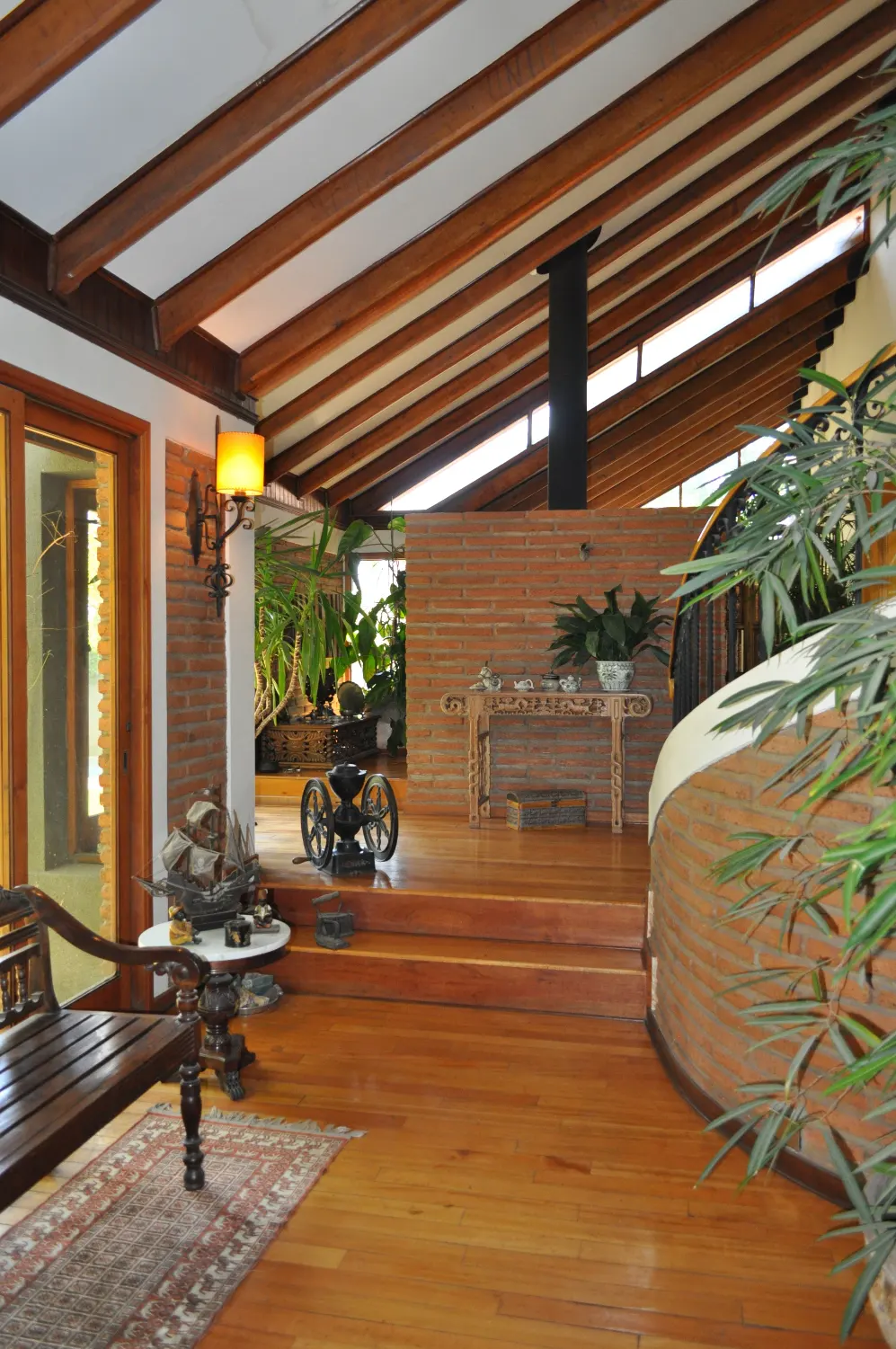 Interior view of a home with wood floors, exposed beams, brick walls, and indoor plants.