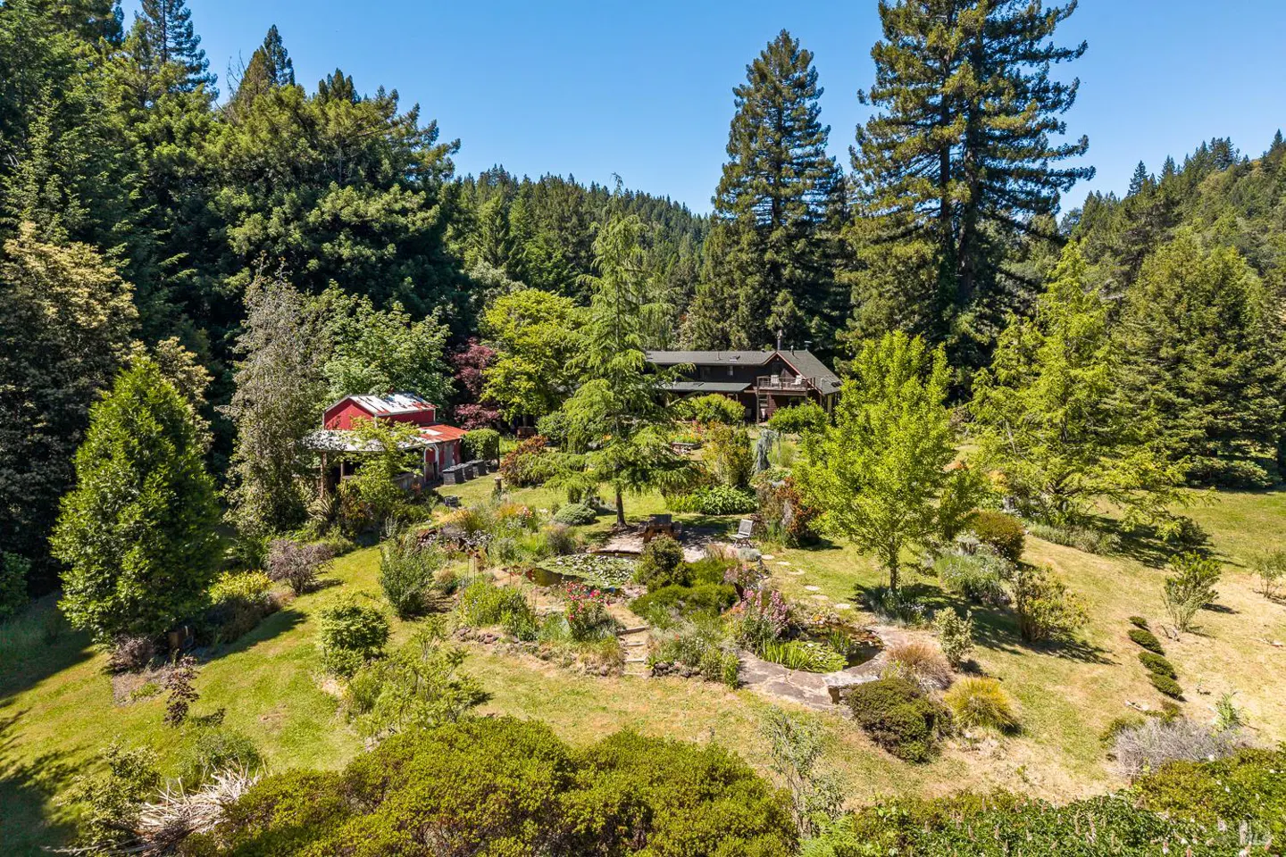 A landscape view of a house and a red barn surrounded by lush greenery and tall trees.