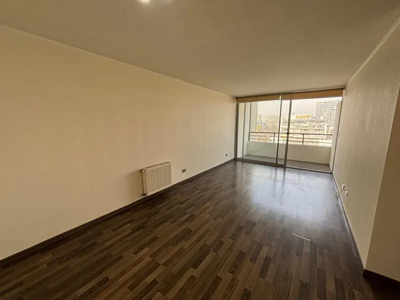 Empty room with dark wood floors, cream walls, and a sliding glass door to a balcony with city views.