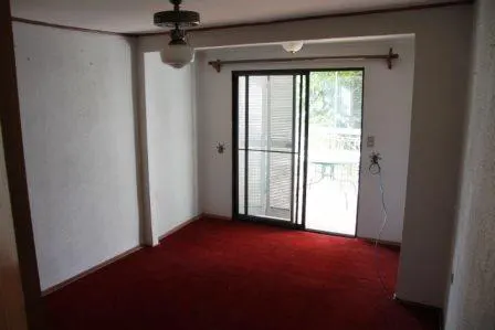 A room with red carpet and white walls, featuring a sliding glass door to a patio. A ceiling fan is visible.