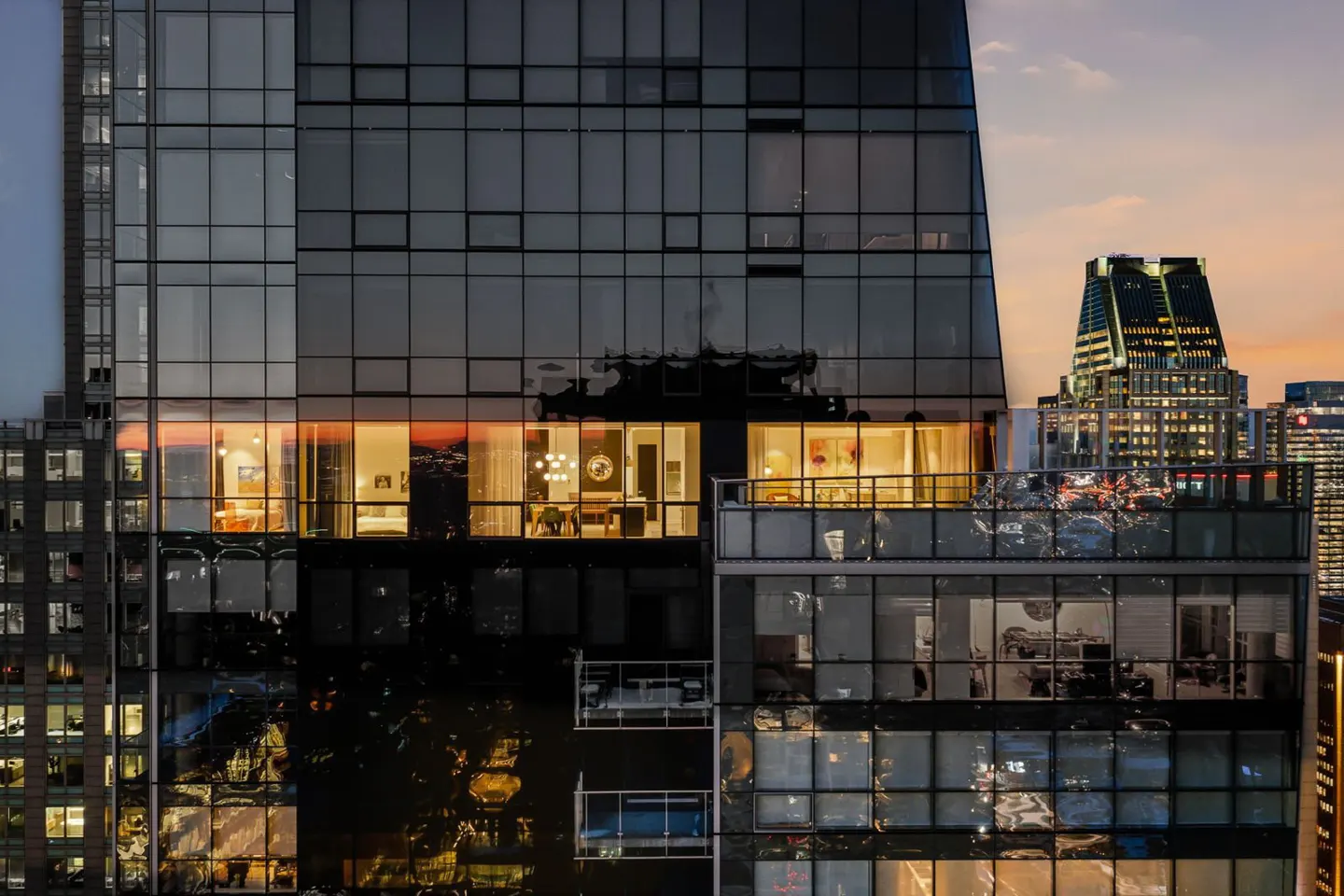 Exterior shot of a modern glass skyscraper at dusk, with warm interior lights visible in some apartments.