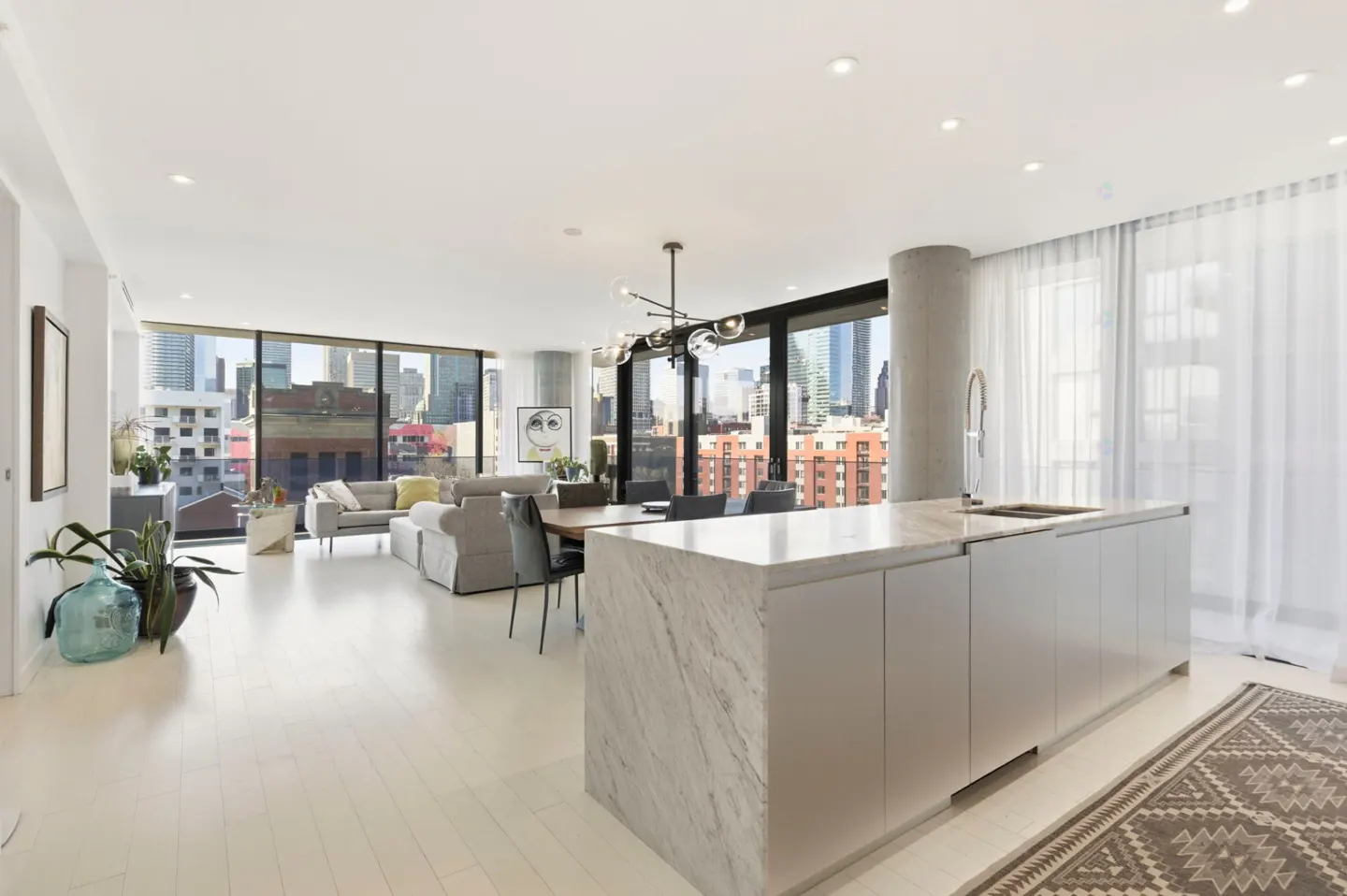 Bright, modern apartment interior with a marble island, dining table, and living area. Large windows offer a city view.