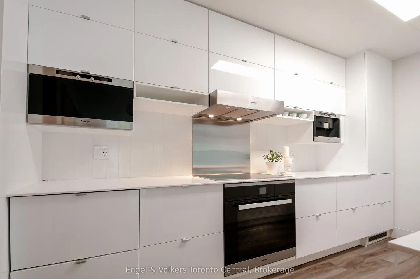 A modern kitchen with white cabinets, stainless steel appliances, and light wood floors.