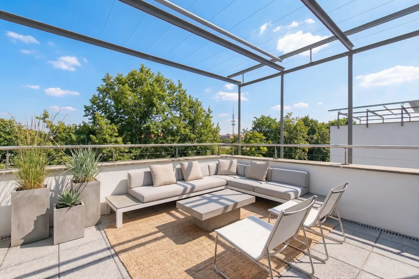 Outdoor patio with gray sectional sofa, coffee table, and white chairs on a woven rug. Green trees and blue sky in the background.