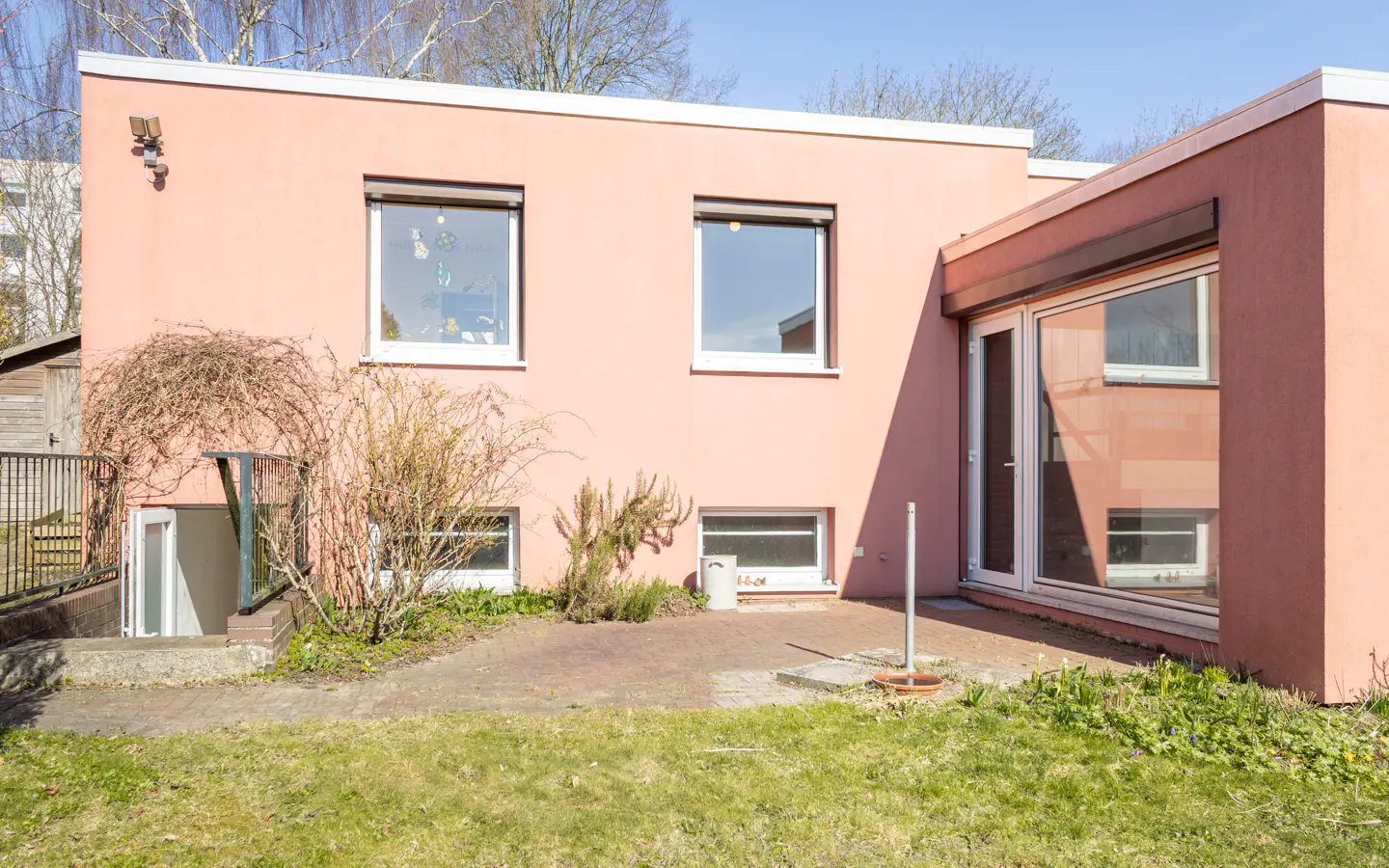 Exterior view of a two-story, salmon-colored house with white-framed windows and a walk-out basement. A brick patio leads to a grassy lawn.