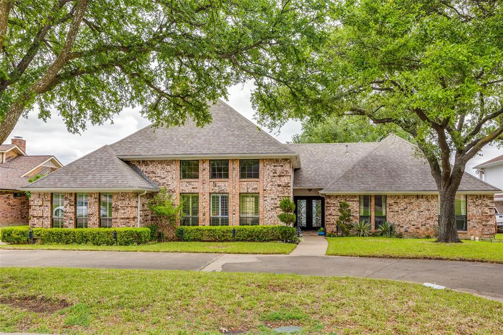 A one-story brick house with a gray roof is framed by green trees and a green lawn.