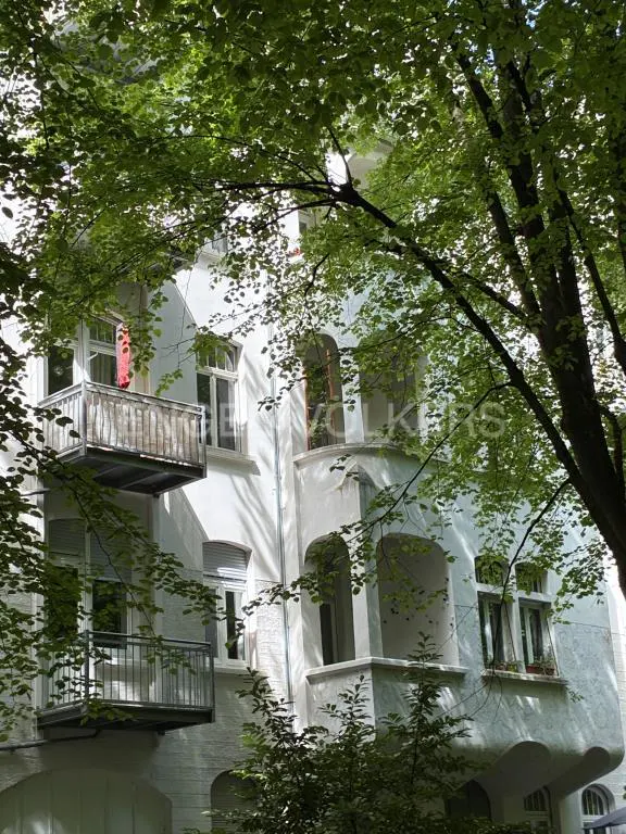 Exterior of a white building with balconies, framed by green trees.