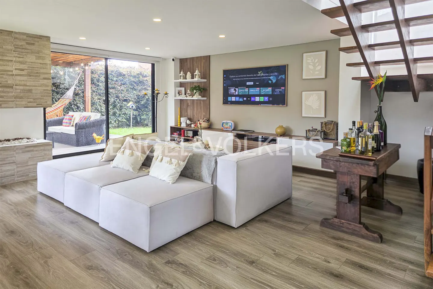Modern living room with a white modular sofa, wood floors, wall-mounted TV, and a wooden staircase leading to a loft.