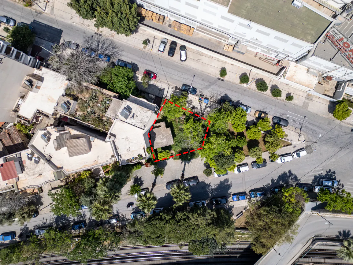 Aerial view of a property outlined in red, surrounded by trees, buildings, and parked cars on a sunny day.