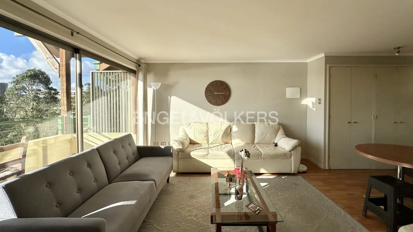 Living room with gray and white sofas, glass coffee table, wood floors, and large windows with a view of trees.