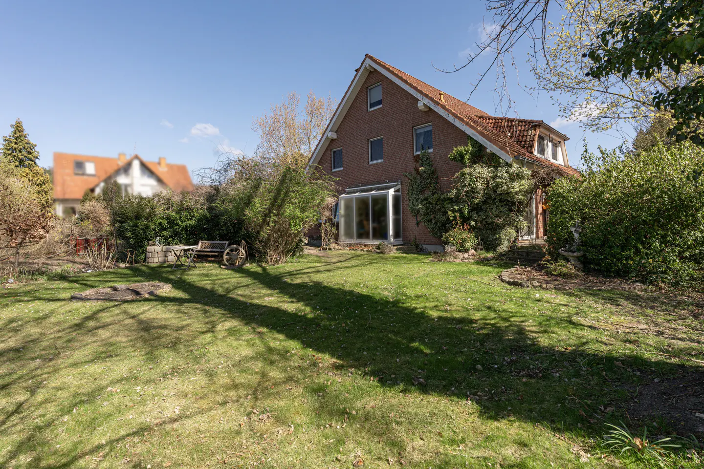 Exterior view of a red brick house with a green lawn and a wooden bench with a wagon wheel.
