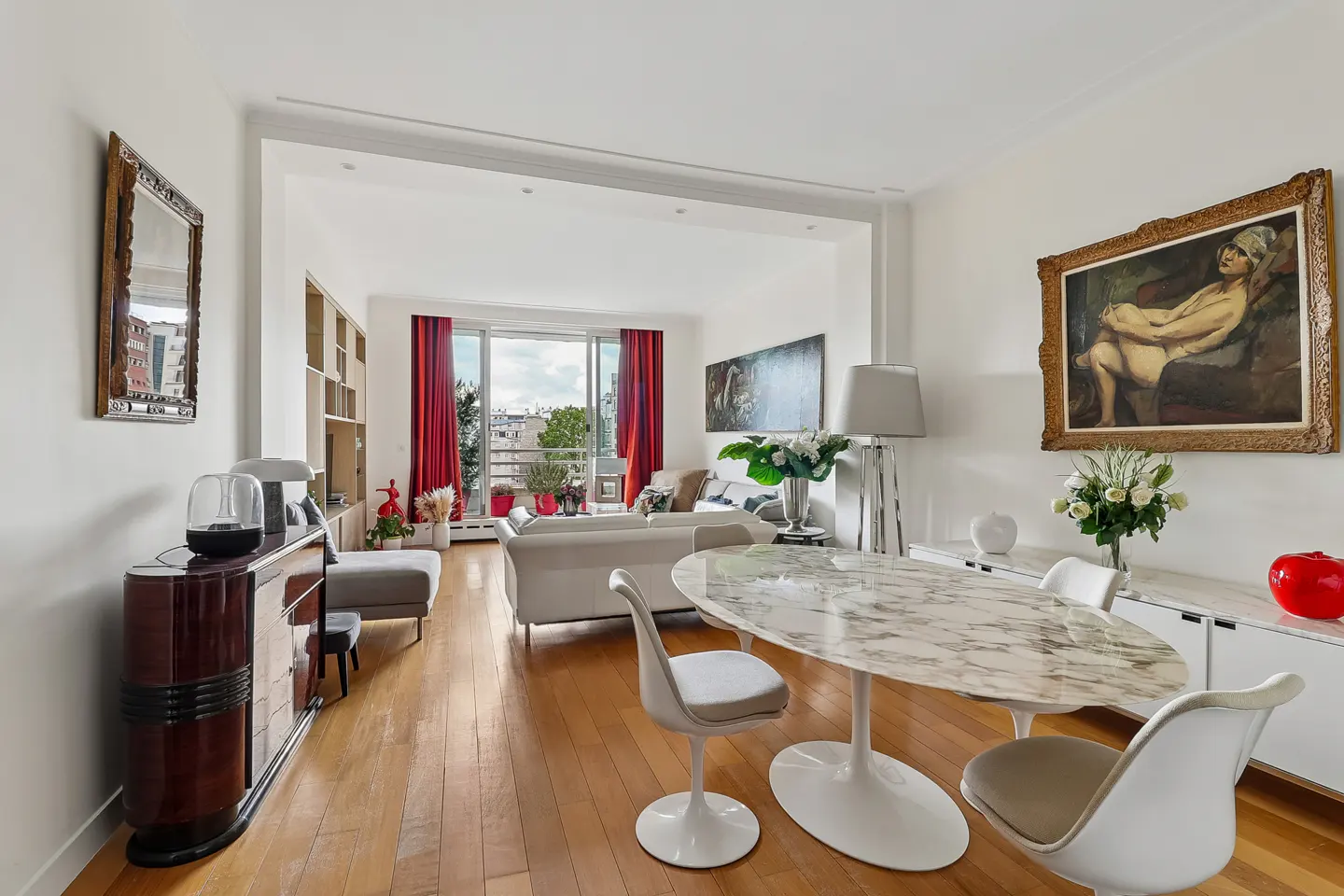Bright, open-concept apartment with wood floors, white walls, and modern furniture. A marble table and chairs sit near a white cabinet with art.