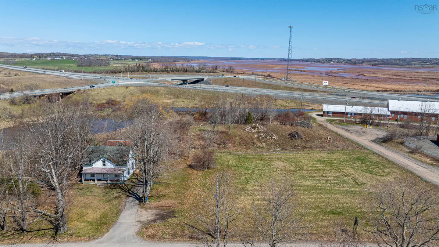 Aerial view of a white house with a porch, a highway overpass, and a red mudflat under a blue sky.