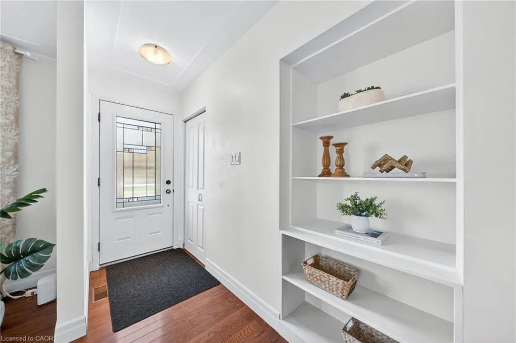 Bright entryway with white walls, wood floors, and a built-in bookshelf. The white front door has decorative glass. A gray rug sits inside.