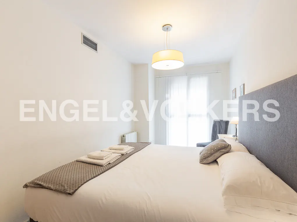 Bright bedroom with white walls, a large bed with white linens, and a gray headboard. A round light fixture hangs from the ceiling.