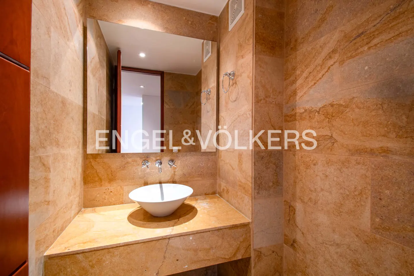 Bathroom with marble walls, a white bowl sink, and a large mirror above the sink.