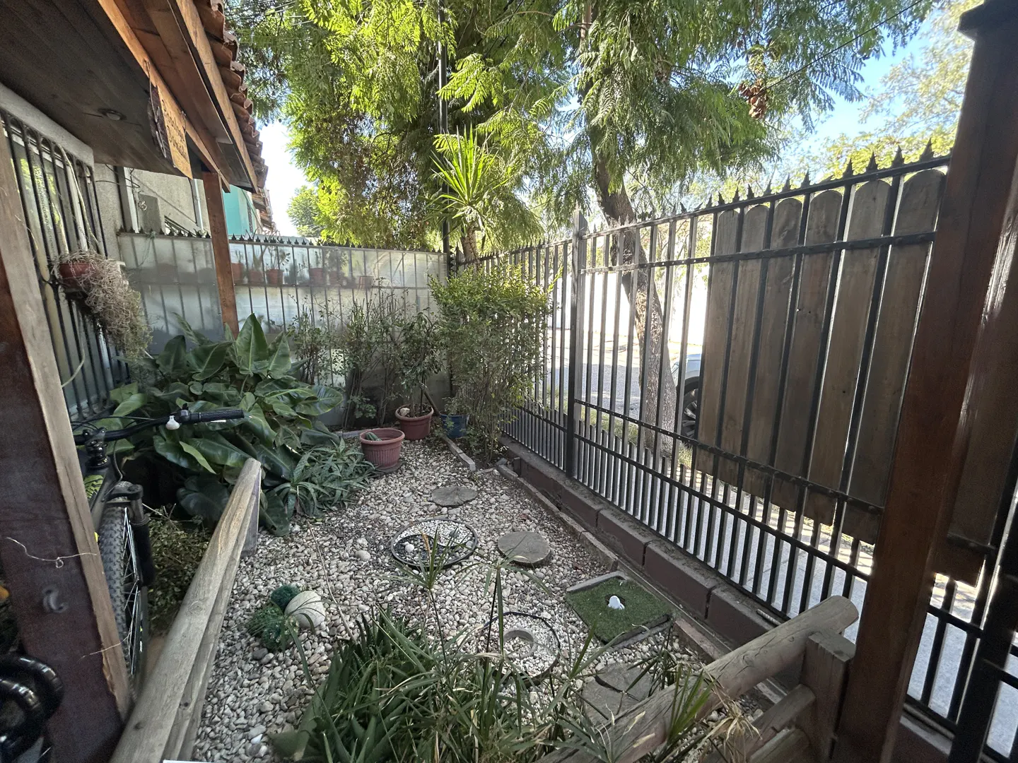A small garden with plants, gravel, and a black metal fence. A bicycle is leaning against a wall.