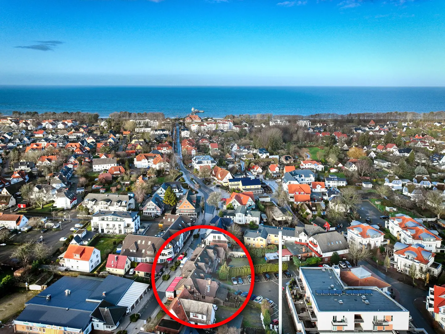 Aerial view of a coastal town with a red circle highlighting a property. Blue ocean and sky in the background.