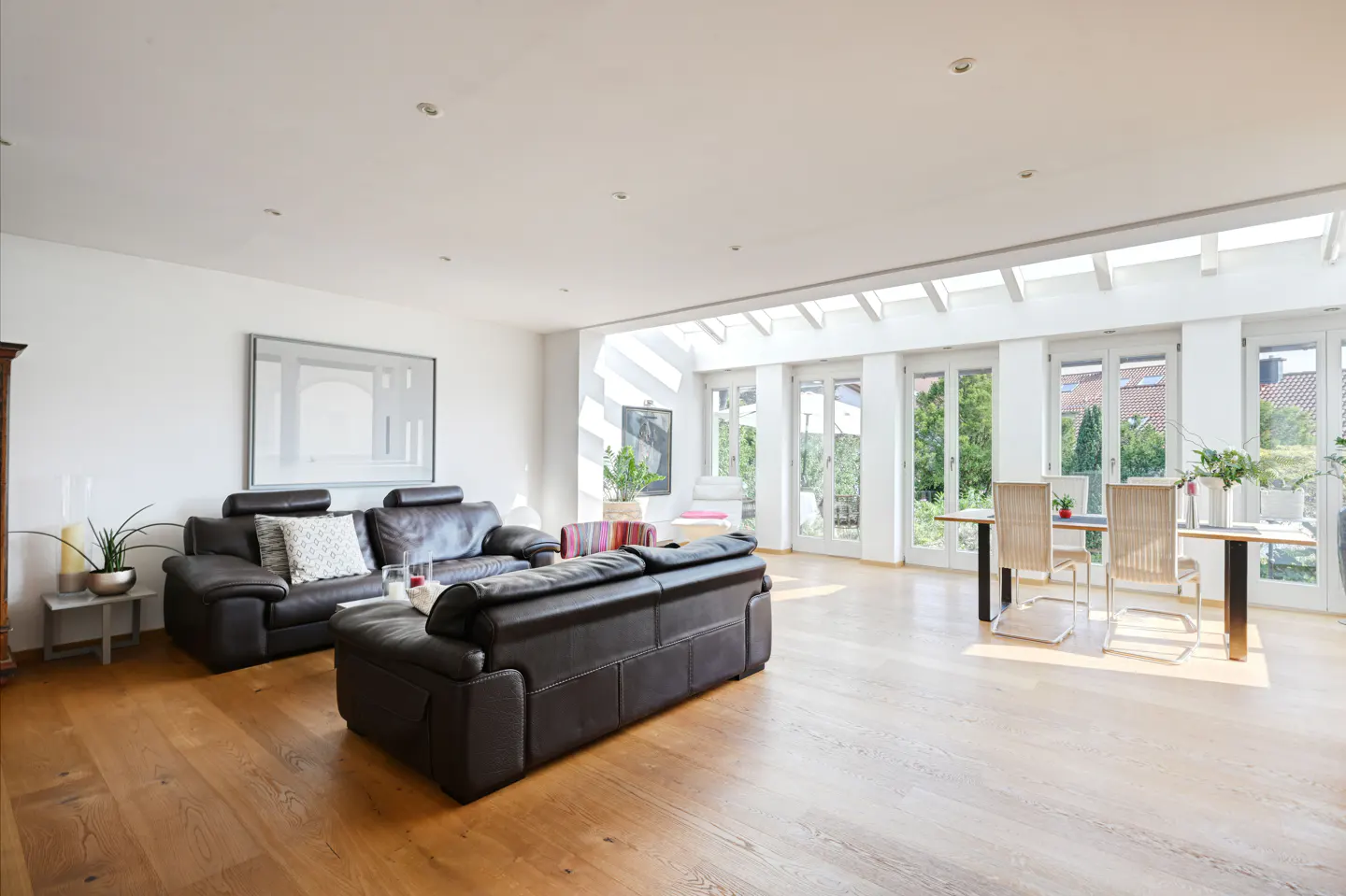 Bright, open living room with hardwood floors, black leather sofas, and a dining table near glass doors to the garden.
