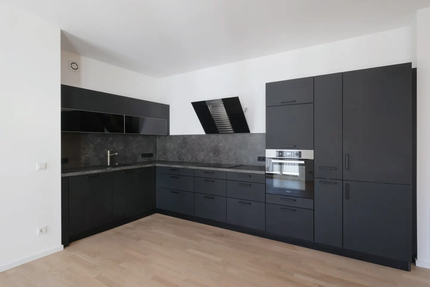 Modern kitchen with dark gray cabinets, stainless steel oven, and light wood floors.