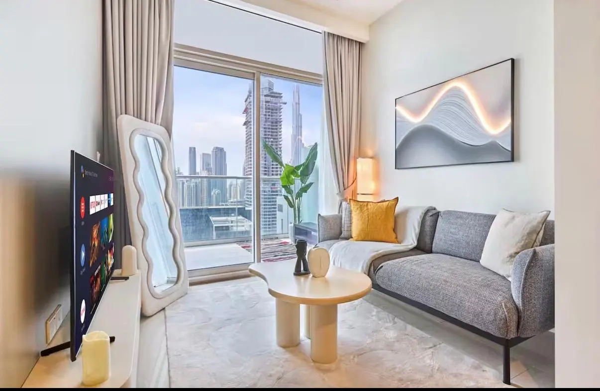 Bright living room with a gray sofa, a unique coffee table, and a large window showing a city skyline.