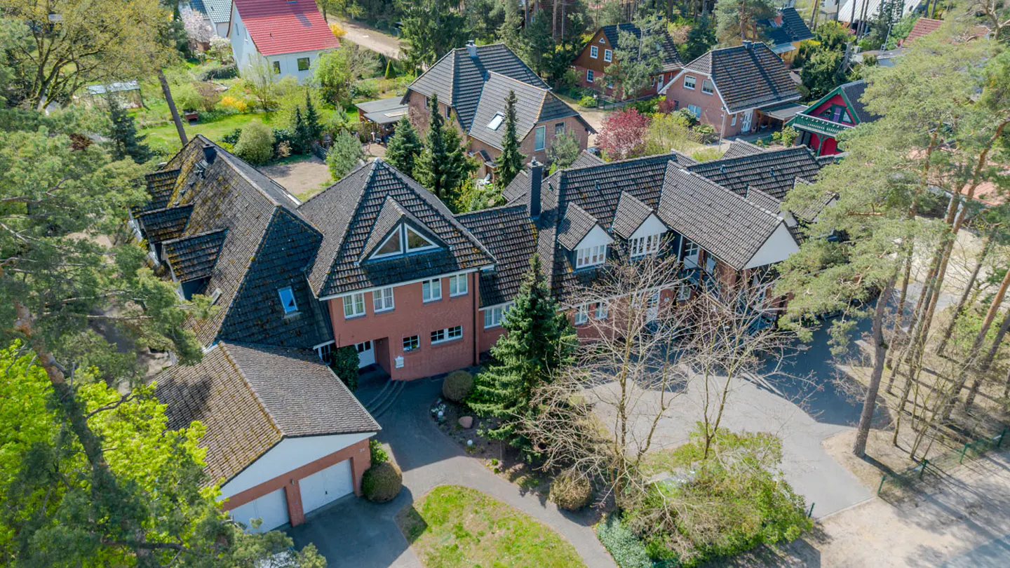 Aerial view of a large, red brick house with a dark gray roof, surrounded by trees and a two-car garage.