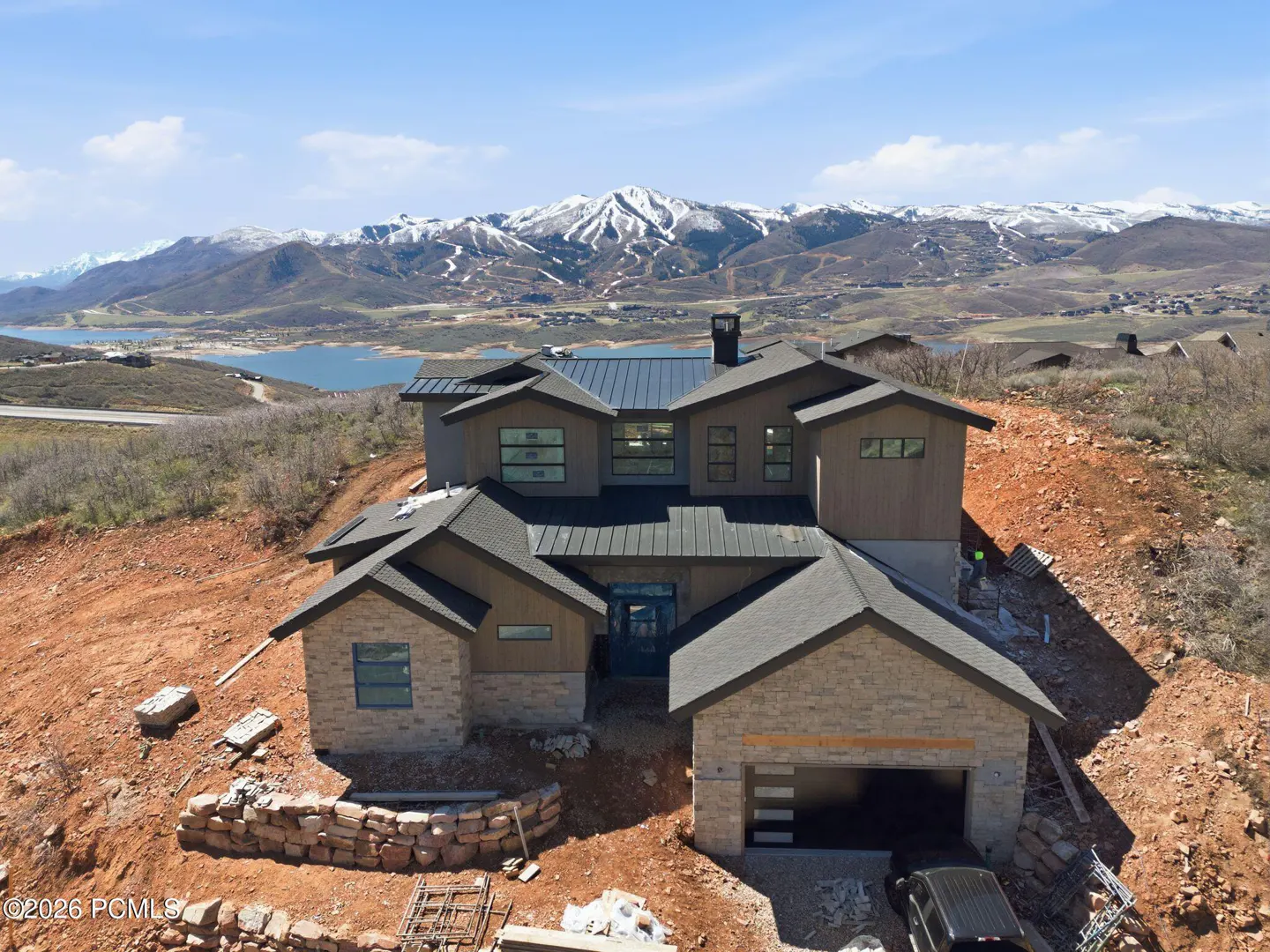 A modern two-story house with a mountain view. The house is made of stone and wood, with a dark roof and a two-car garage.
