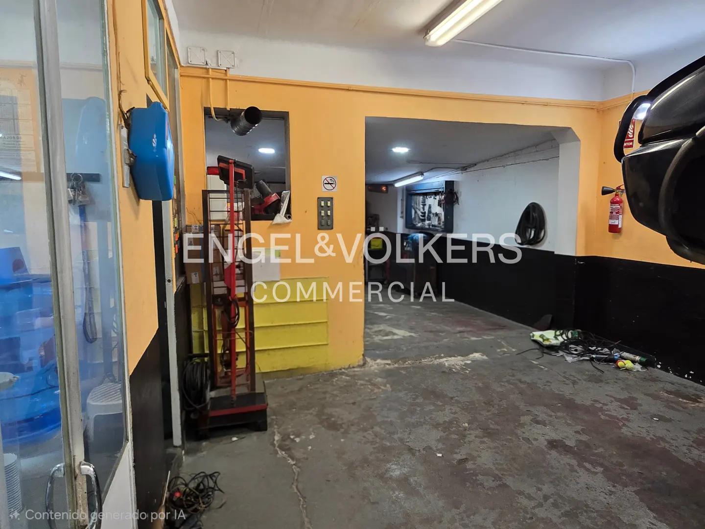 Interior of a commercial garage with yellow and black walls, concrete floor, equipment, and a fire extinguisher.
