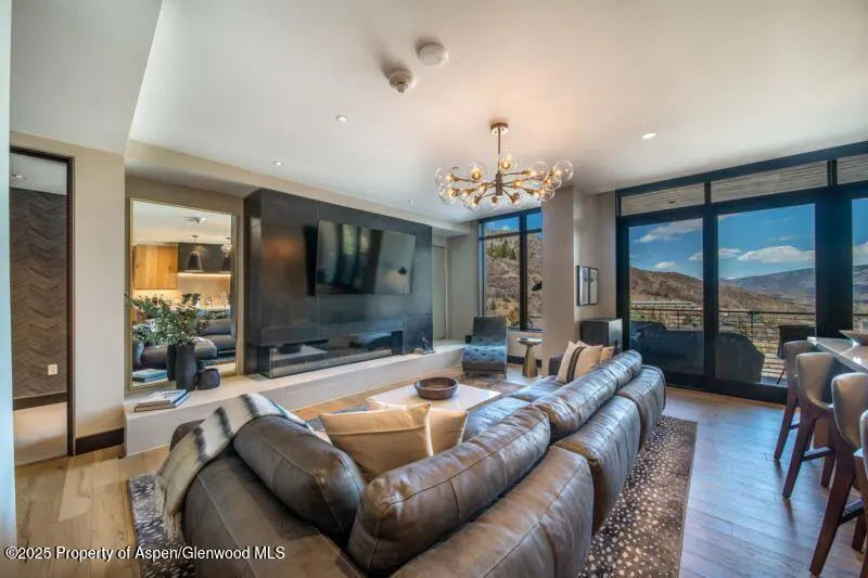 Modern living room with a large grey sectional, a dark fireplace wall with a TV, and floor-to-ceiling mountain views.