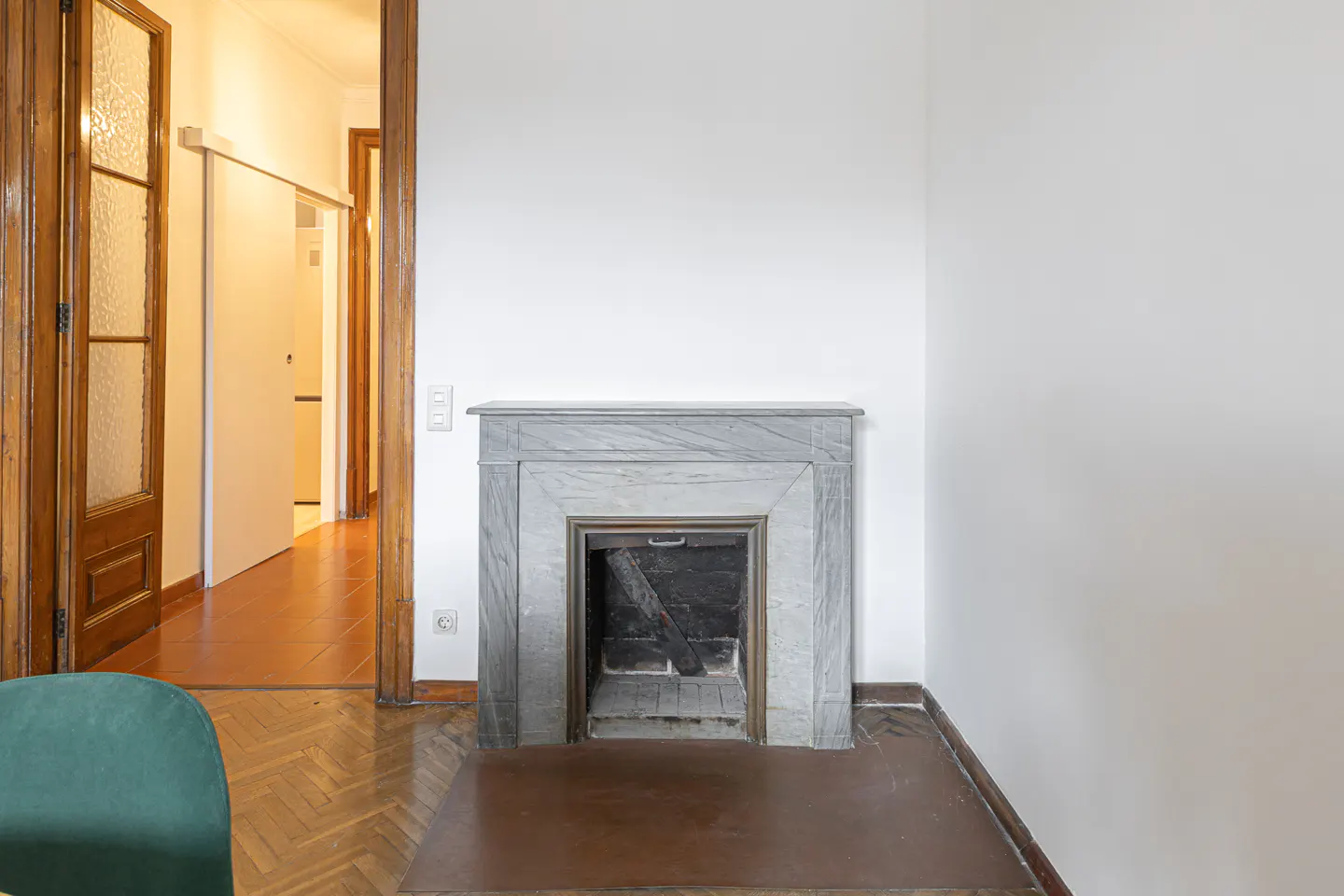 A room with white walls features a marble fireplace. A doorway with a wooden frame is visible on the left.