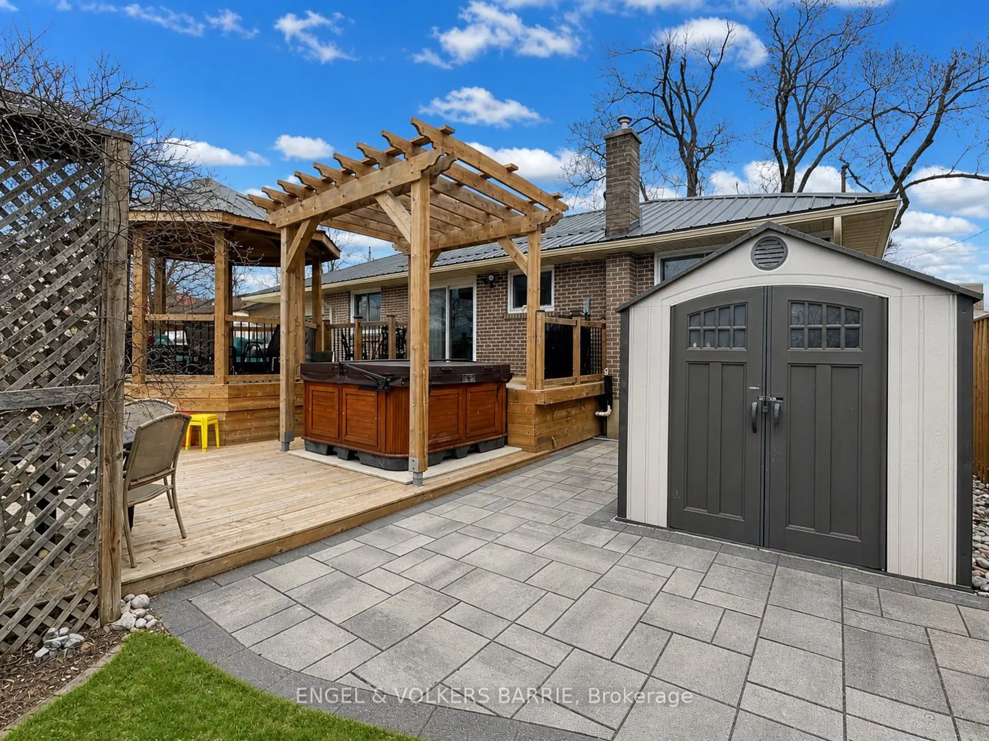 Backyard with a hot tub under a pergola, a gazebo, a shed, and a stone patio.